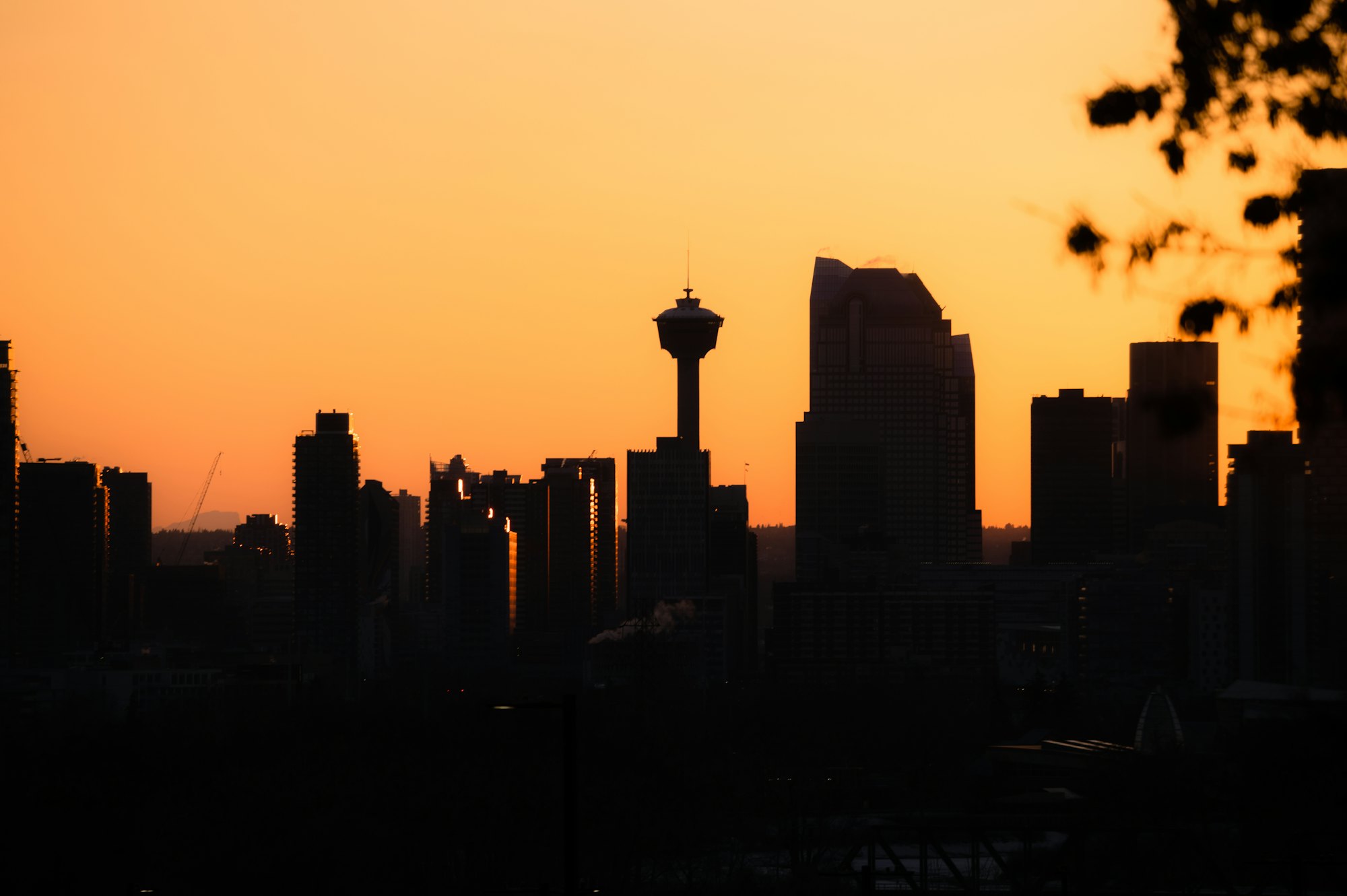 Downtown Calgary in silhouette against an orange sky at dusk, with the Calgary Tower at the centre.